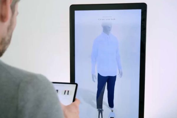 Man holding using PICTOFiT Smart Mirror to try on a blue shirt and black pants.